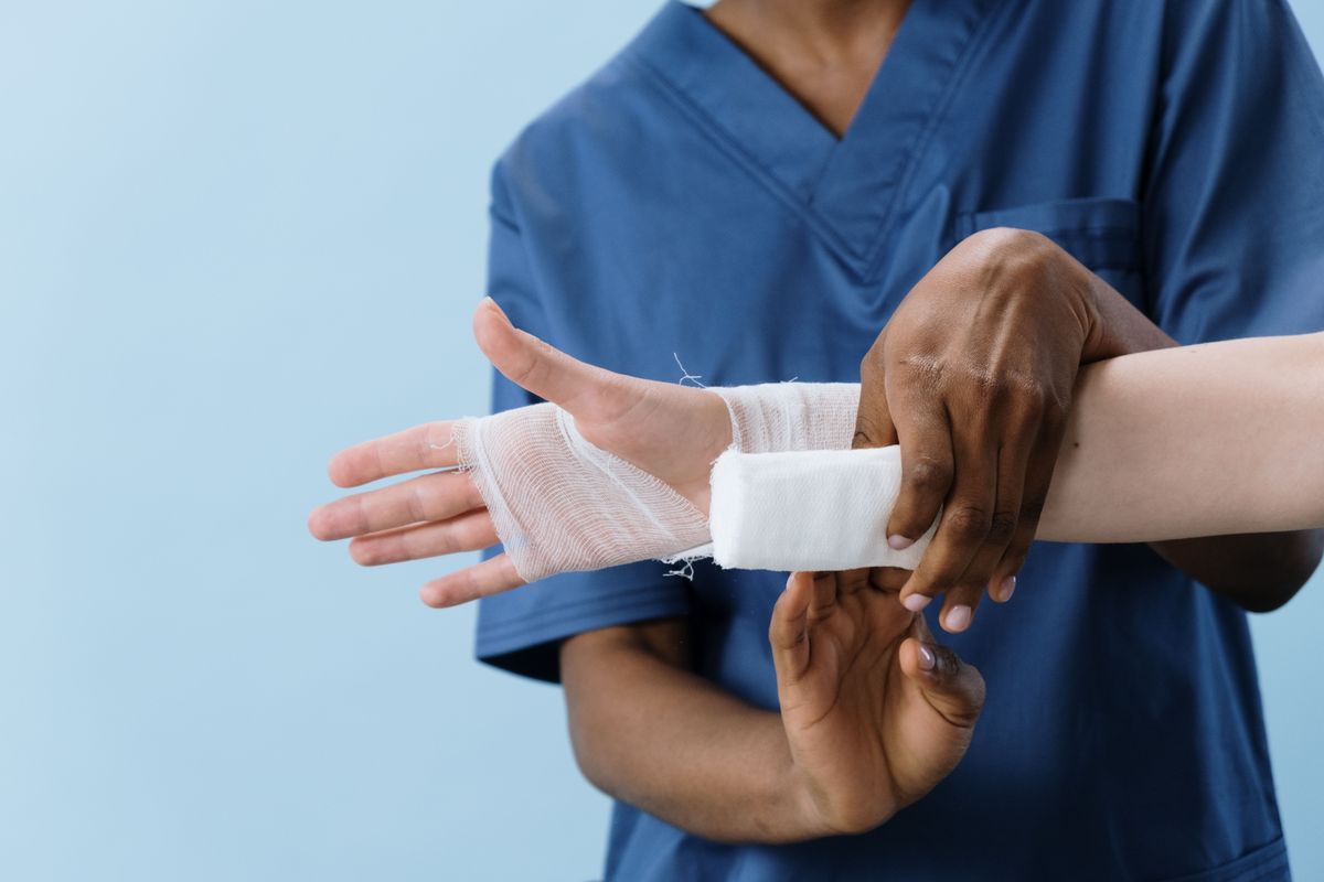 Een verpleegkundige in een blauw uniform legt een verband aan rond een pols.